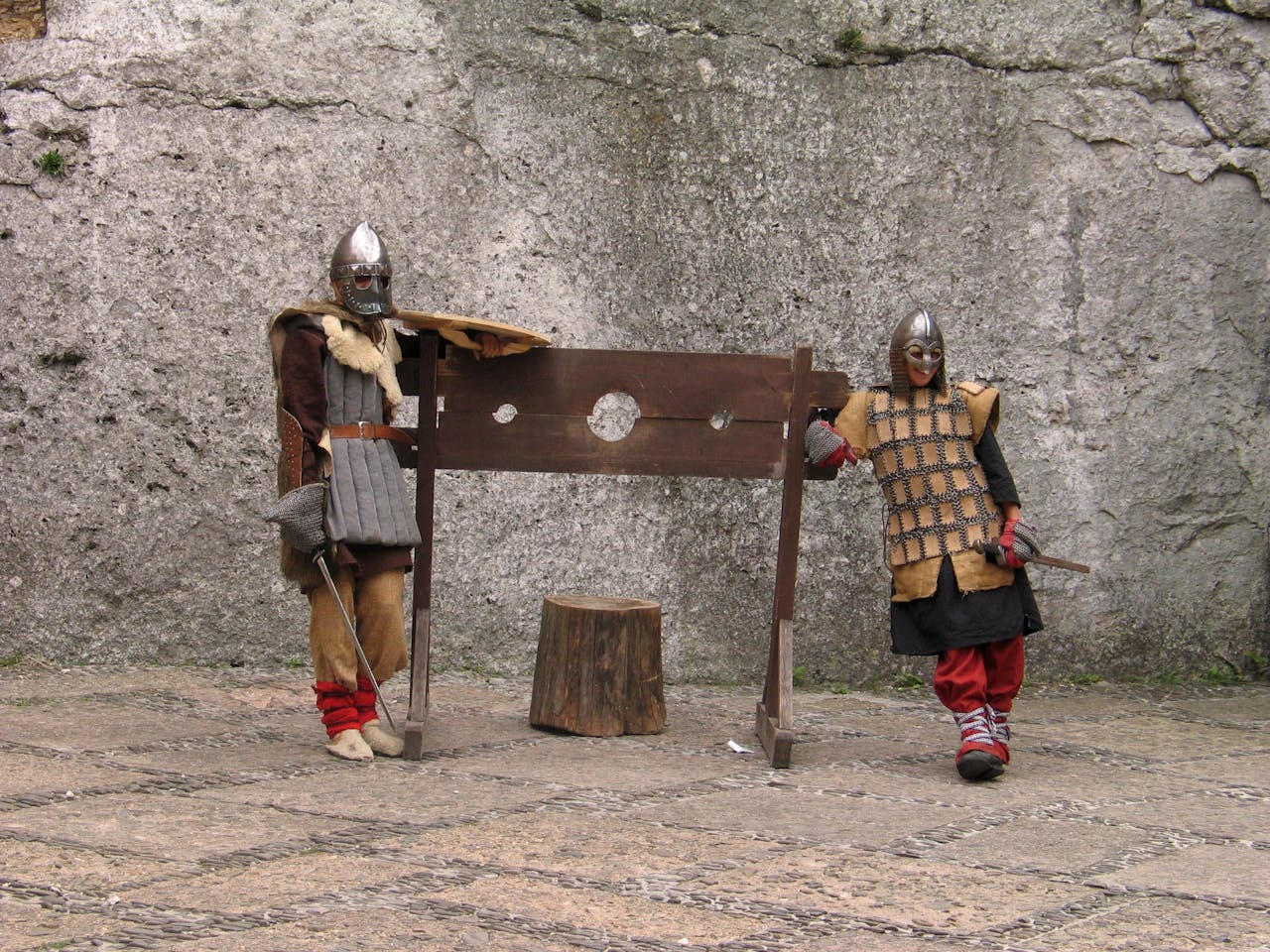 Two medieval knights in armor posing with stocks outdoors, showcasing historical costumes.