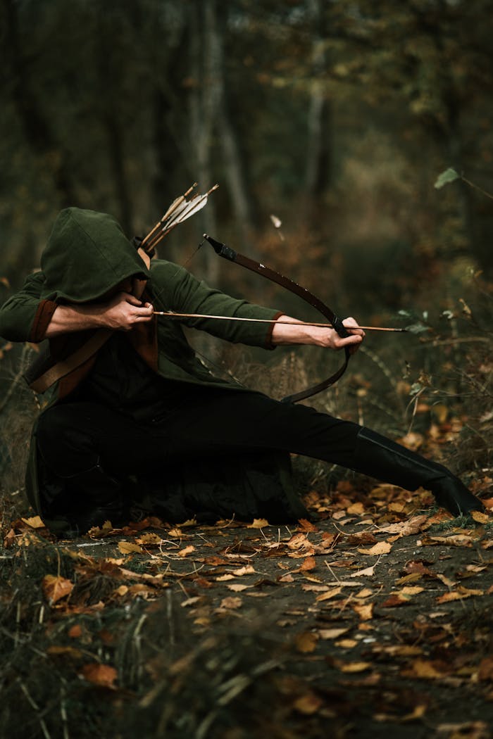 A hooded archer striking a dramatic pose with a bow in a serene autumn forest setting.