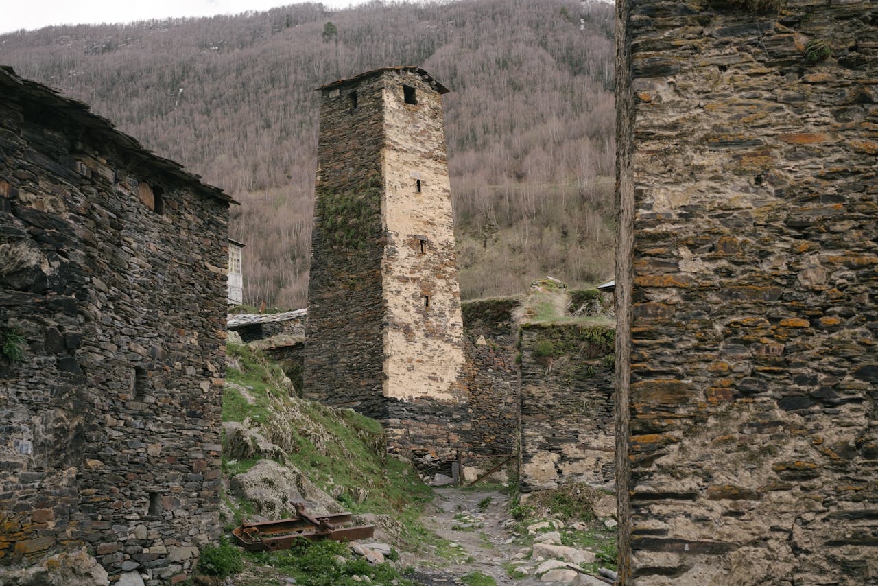 A historic stone tower amidst medieval structures in a mountainous landscape.